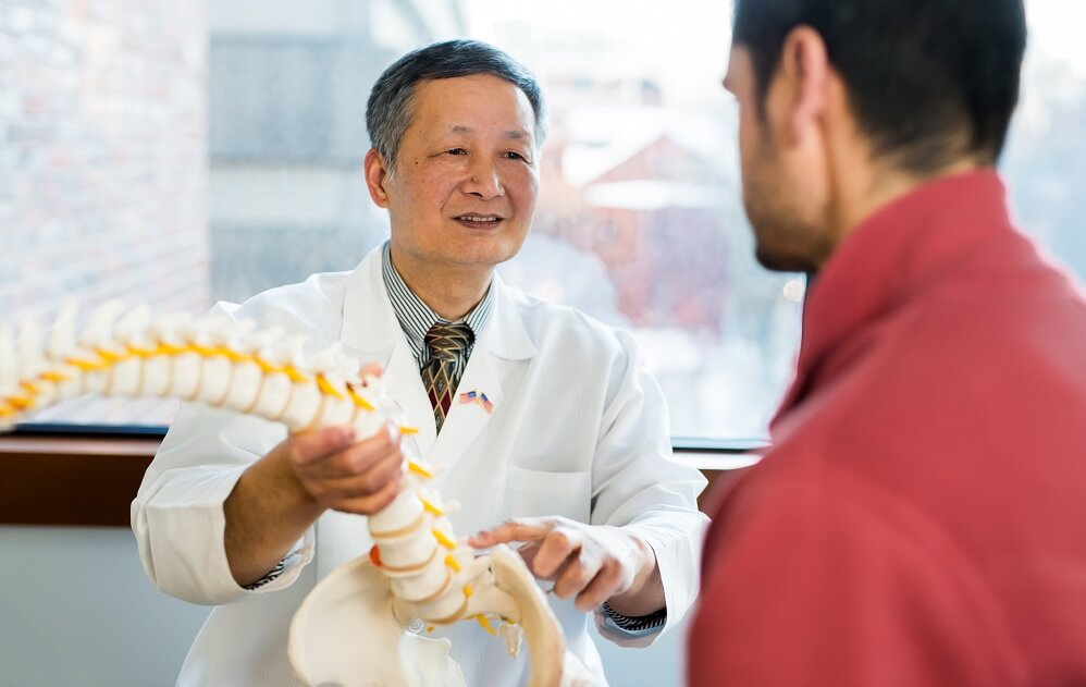 Jianren Mao, MD, PhD describes a replica spine to a patient Jianren Mao, MD, PhD describes a replica spine to a patient